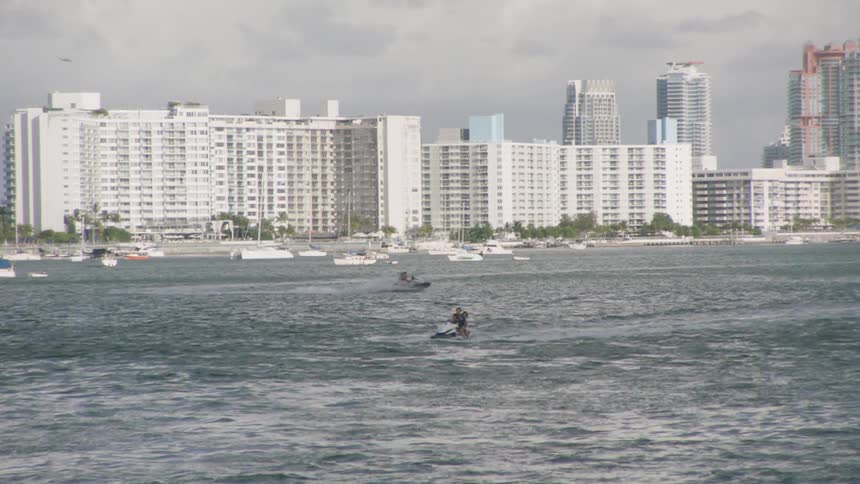 People ride jet skis on a city coastline