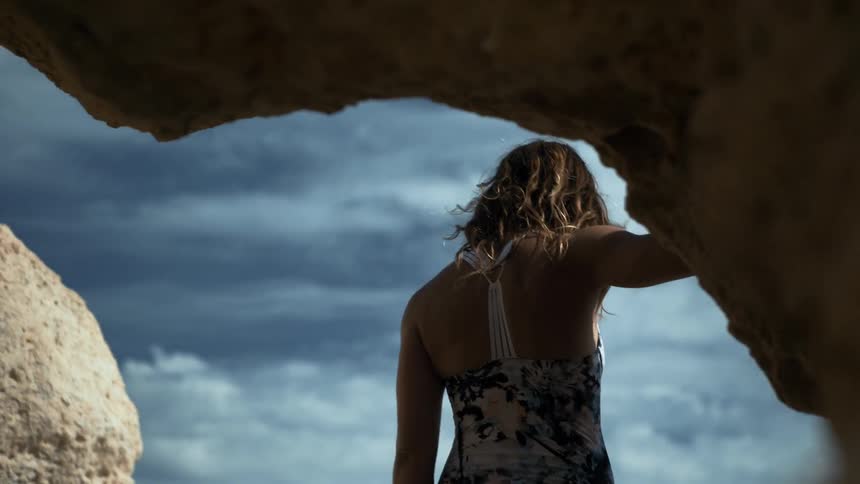 A woman leans against the rocks of a cave exit