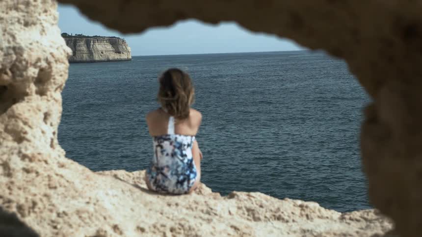 A woman sits on a rocky beach