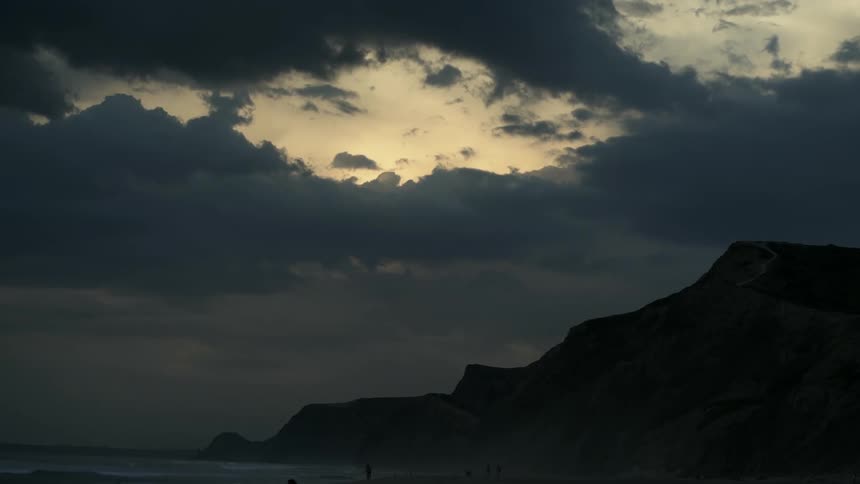 The sun is setting as the dark clouds move over the mountain