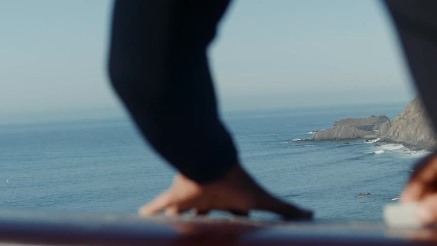 A person is polishing their surfboard by the shore