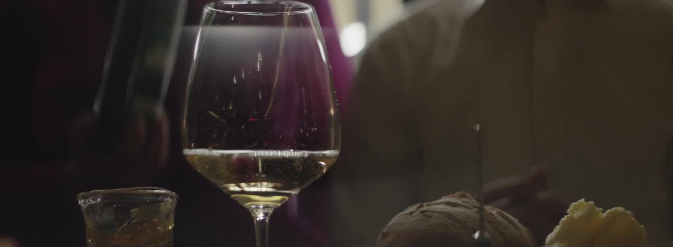 A man and woman sit at a table with wine and food