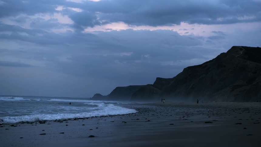 People stand in the distance on the shore at sunset