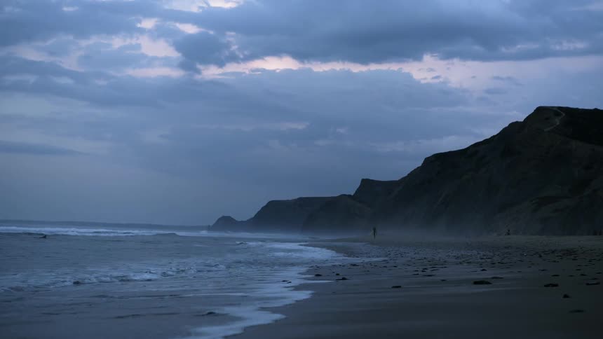The waves crash against the shore as people stand in the distance