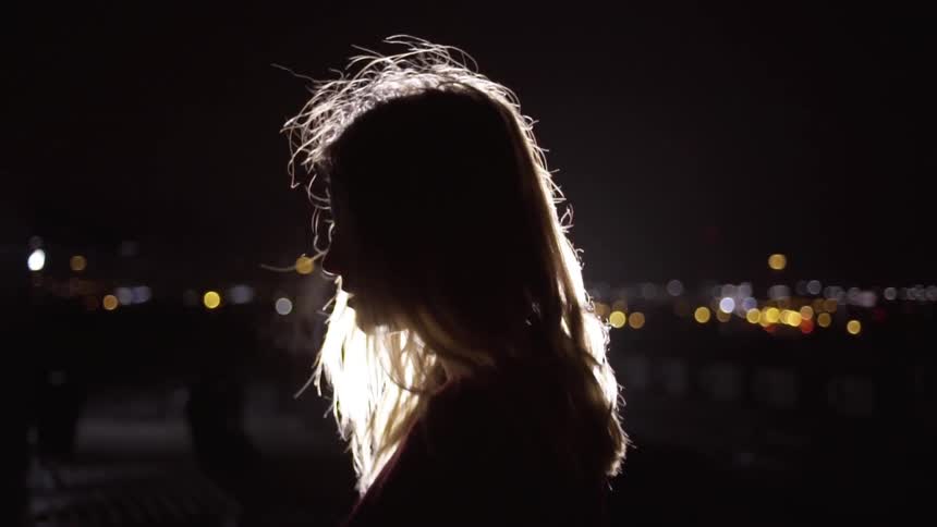 Woman stands in the dark near the city