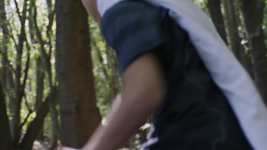 A boy with a towel cape runs through the woods