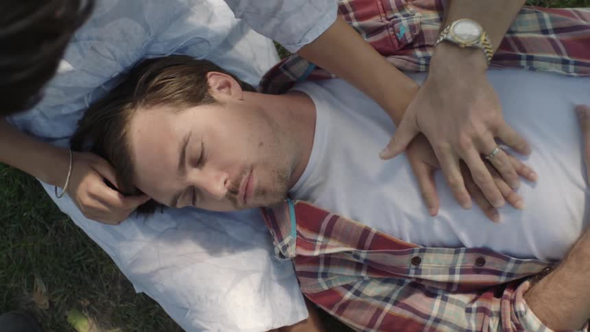 Man lays in a woman's lap and holds her hand on his chest