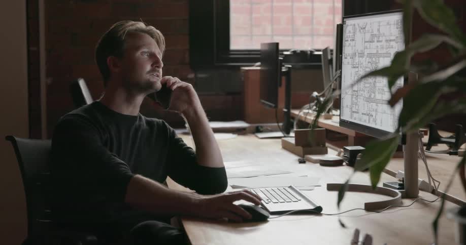 A man talks on a phone while working at a desk