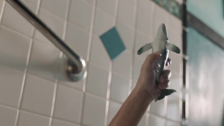 Someone sitting in the bathtub, holding a toy shark and pretending like it is flying through the air