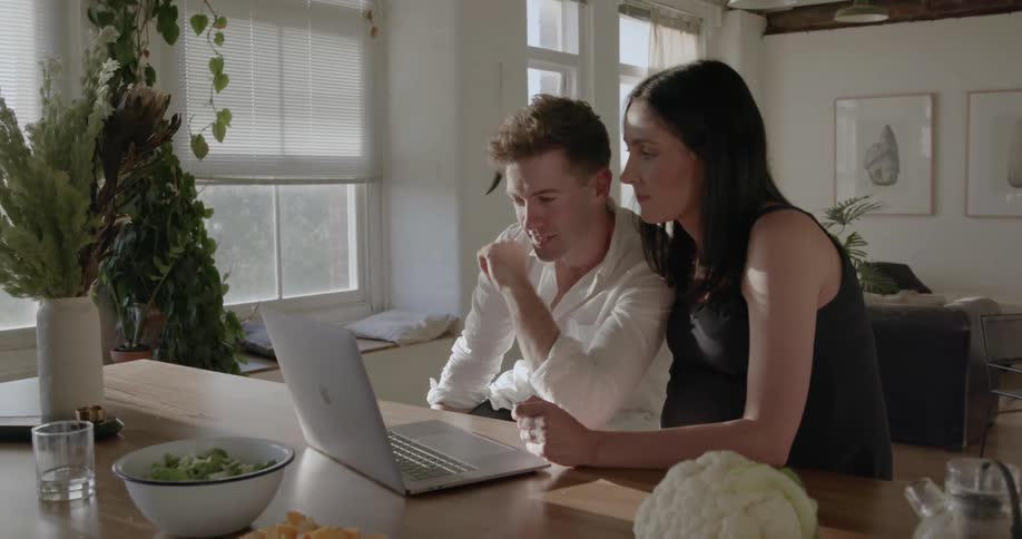 Man and woman sit in front of a laptop smiling