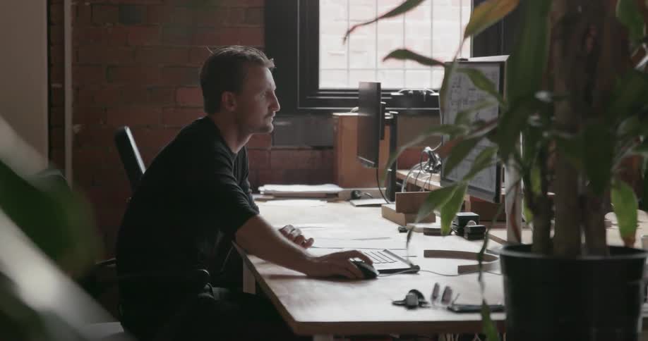 A man leans over his desk using the computer