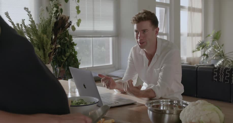 A man uses a laptop and talks in the kitchen