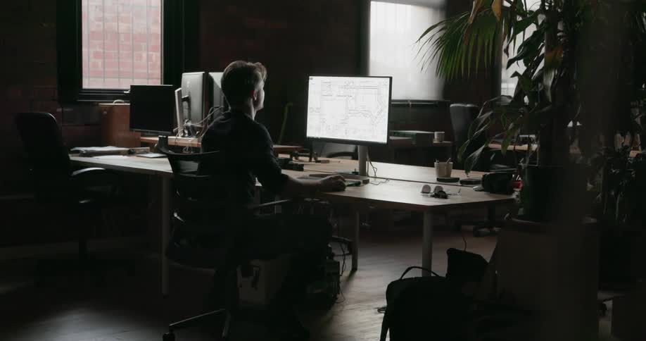 A man is working on the computer in a dark office