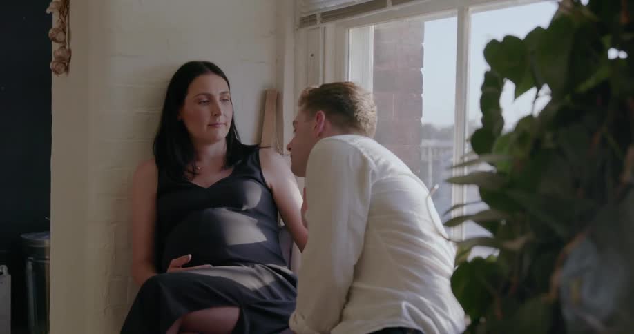 Man kisses a pregnant woman while sitting near a window
