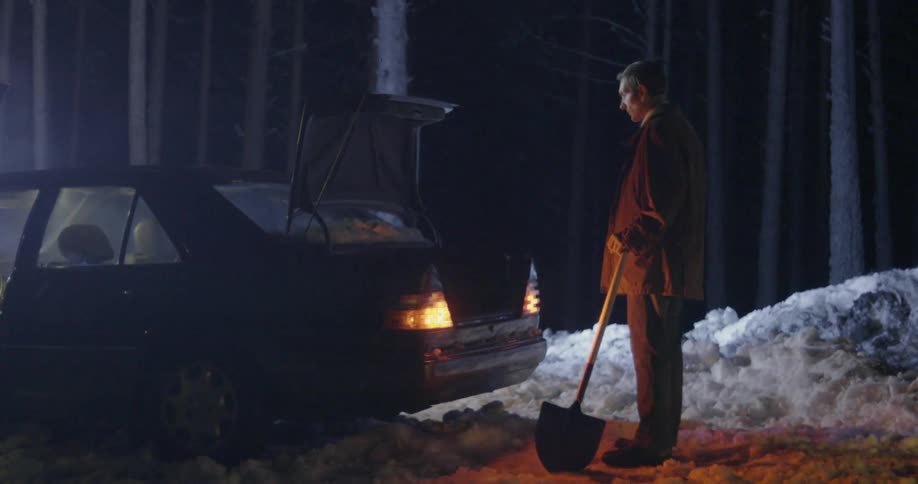 Man holds a shovel as he stands behind a car with its trunk open