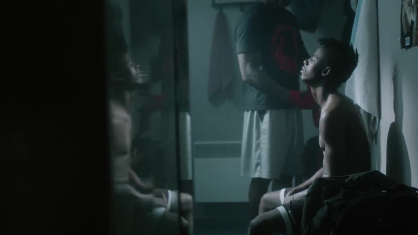 A man sits in the locker room tossing his gloves up and down