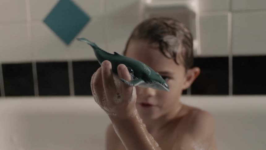 A young boy plays with a toy whale figure in the soapy bathtub