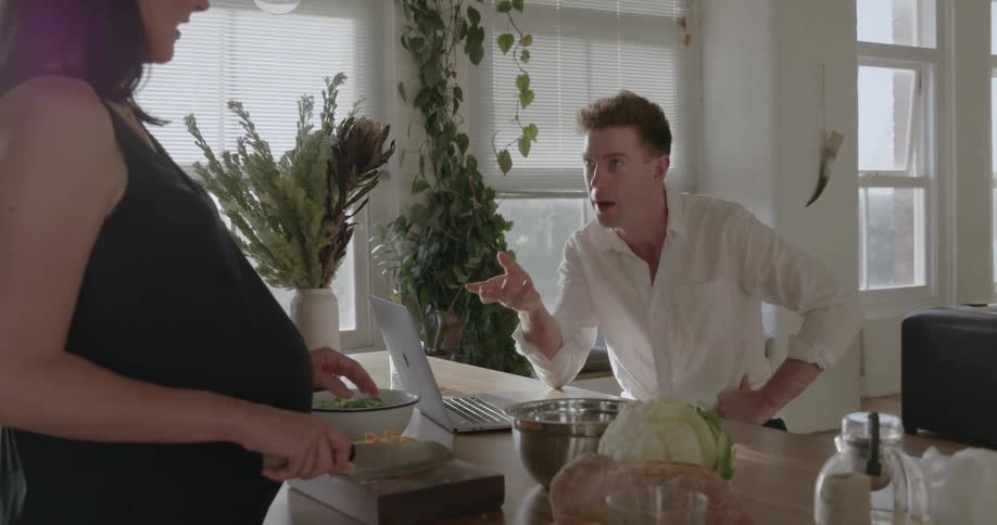 Man sits in front of a laptop talking to a woman who is cutting fruit