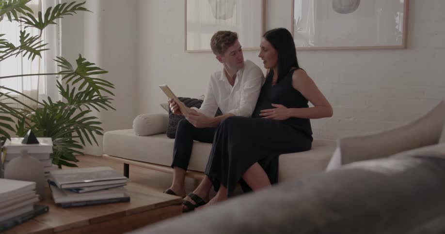 A man and pregnant woman sit on a couch together