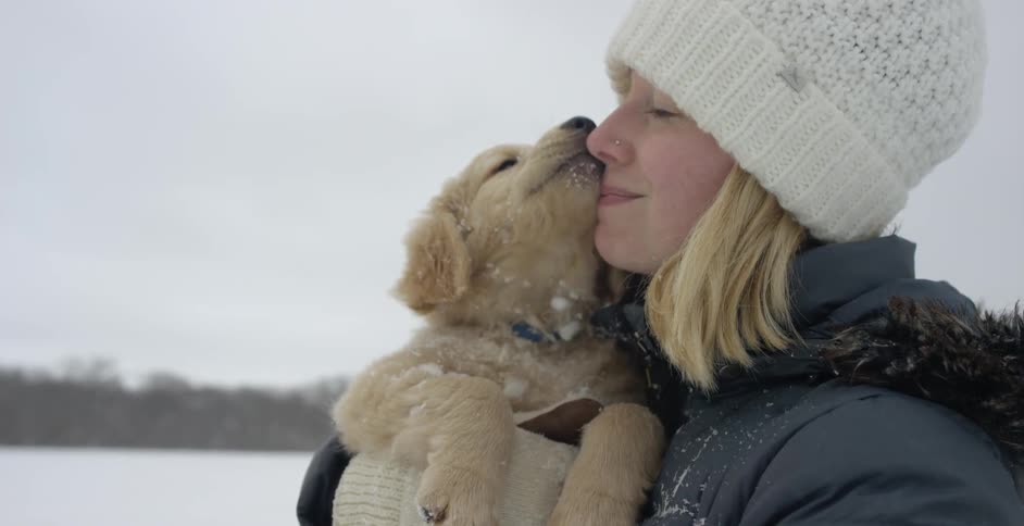 Woman stands outside in the snow holding a dog