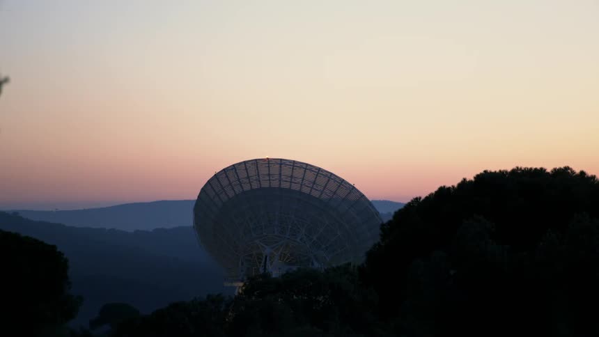 The sun is setting behind the large satellite dish