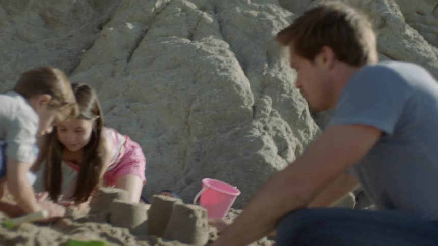 A man and two children building sandcastles next to sand dunes