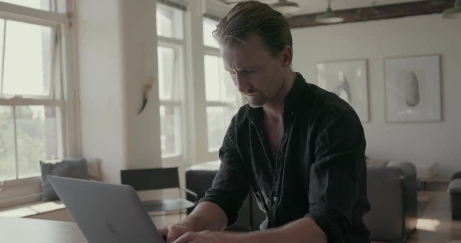 A man working on a laptop inside a home is turning from staring out the window