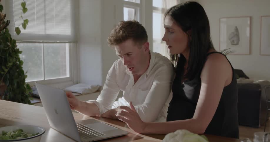 A man and woman talk and work on a laptop