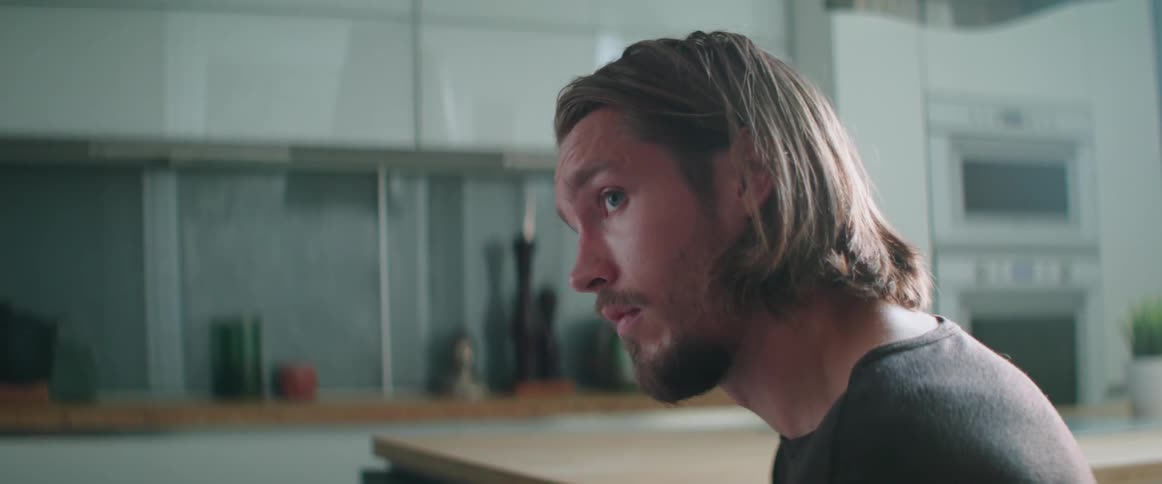 Profile view of a serious young man sitting and listening inside modern kitchen.