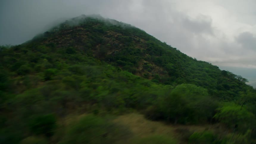 Flying over green forested mountain covered by fog and clouds