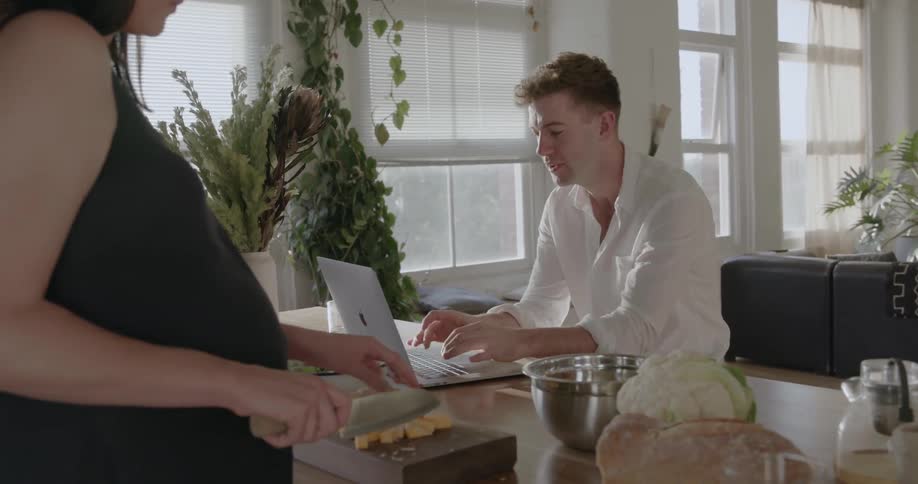 Man types on a laptop as a he talks to a pregnant woman