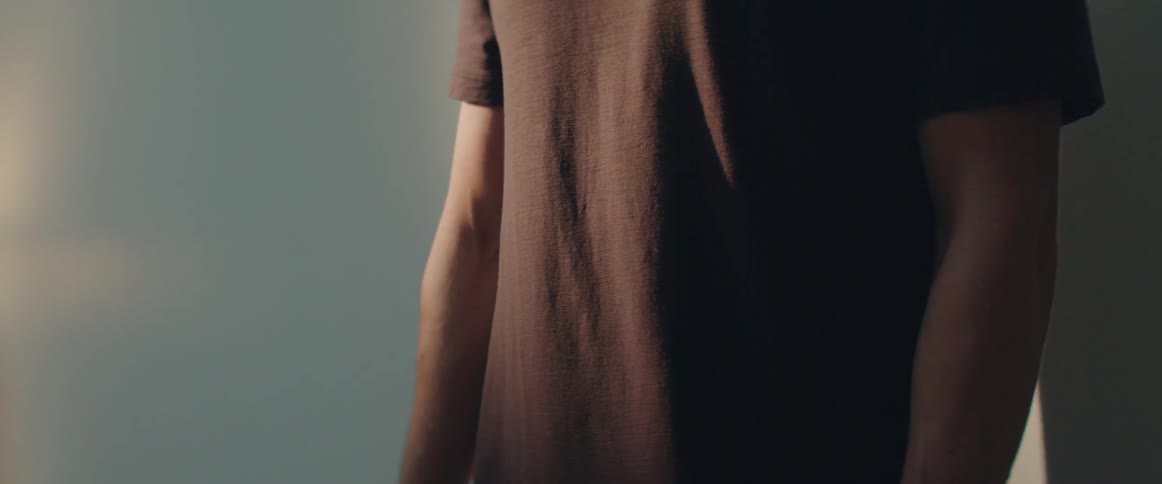 A person wearing a casual brown shirt stands quietly under warm atmospheric lighting.