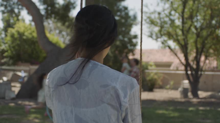 Woman sitting on a swing watching her family play in the yard