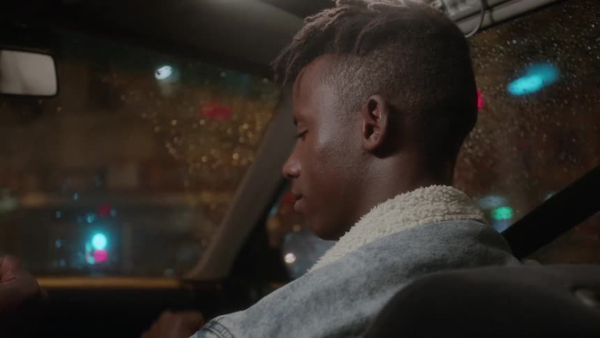 A man looks to the side and taps a man's hand as they drive
