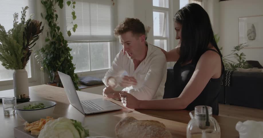 A man touches a pregnant woman's stomach while they look at a laptop