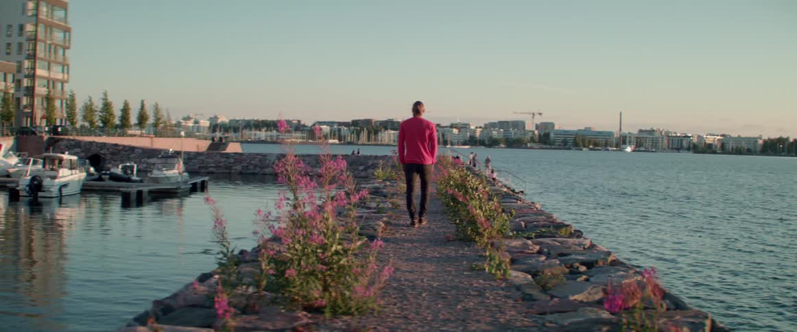 Wide shot of a man walking away down a stone pier by city.
