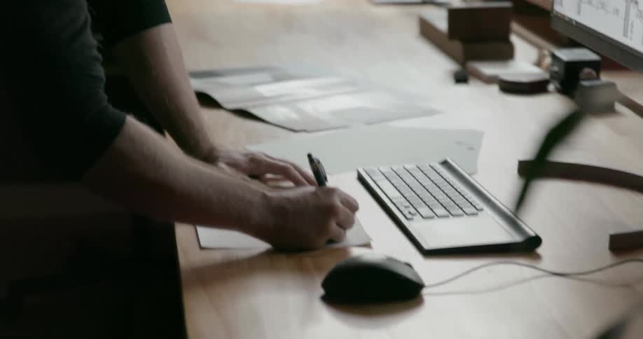 A man works at a computer, and writes something down