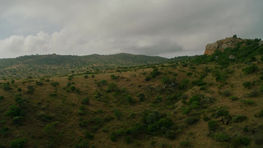 Moving aerial view of some green and brown wilderness in a somewhat hilly area on a cloudy day