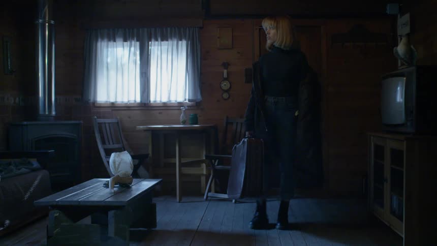A woman enters the dark room carrying a suitcase