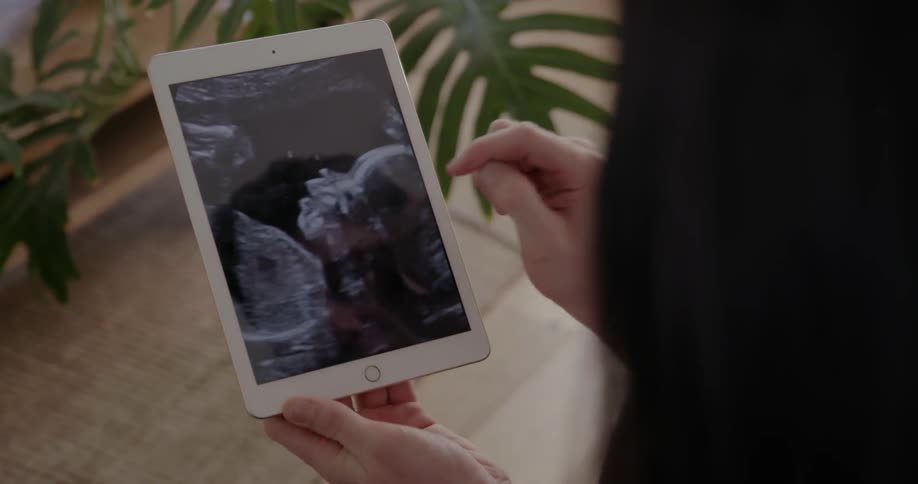 A man zooms in on the ultrasound image of a baby on a tablet