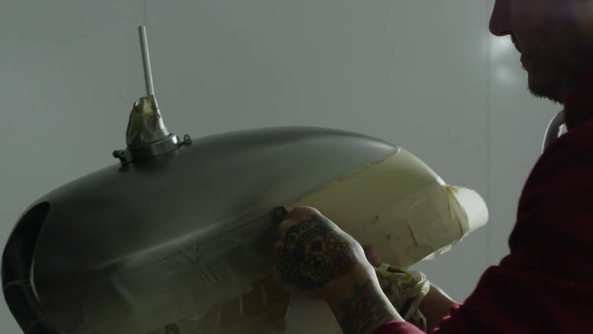 A man is removing tape from a motorcycle part in a workshop in daylight