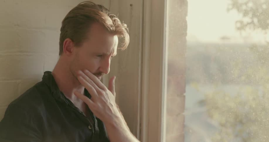 A man types on a laptop on a window seat