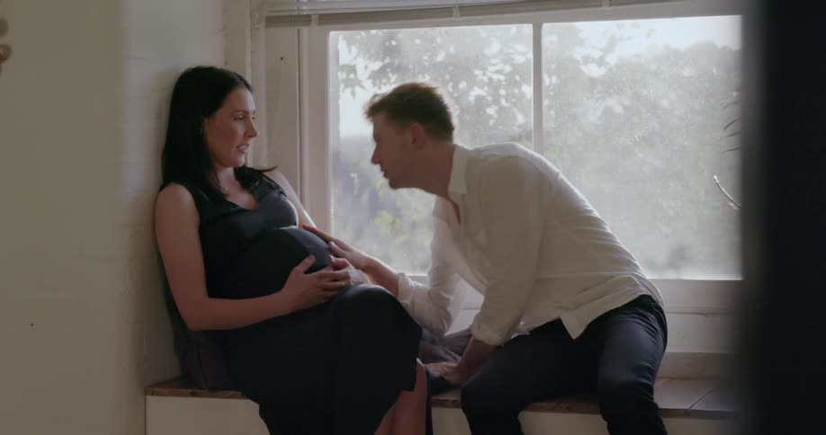 A man leans over and kisses a woman's pregnant belly