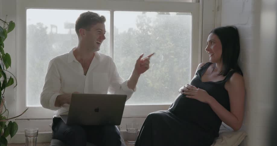 A man uses a laptop as he talks with a woman by the window