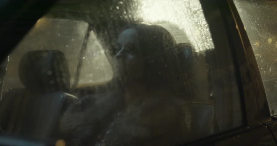 Woman sits in a car with rain streaked windows at night