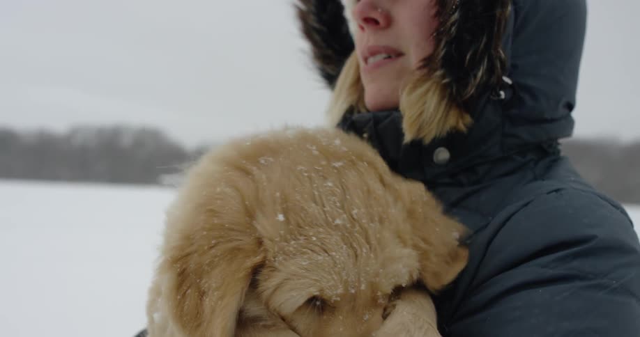 A woman holds her dog as it snows