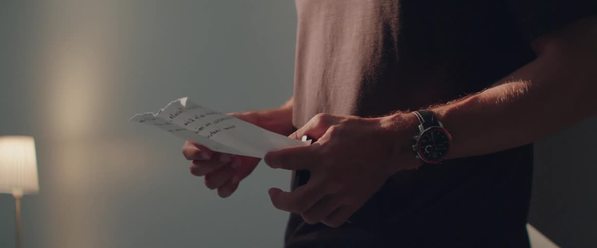 A man wearing a wristwatch carefully handles an important note during the daytime.
