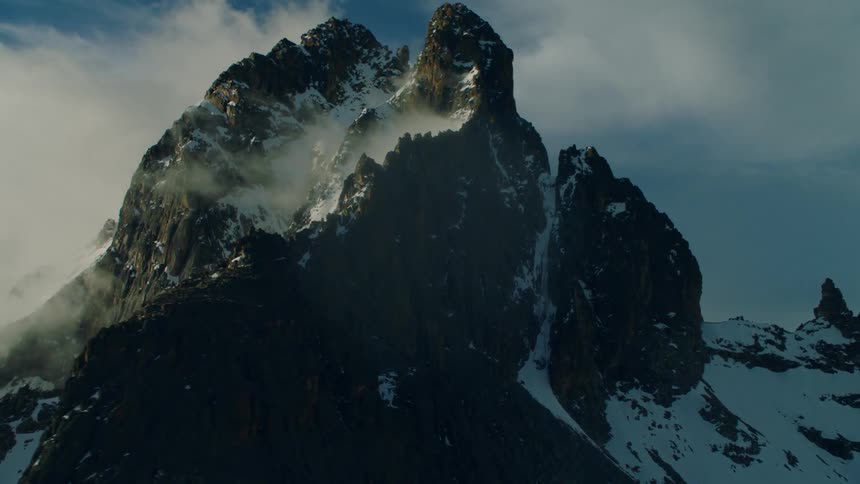 Clouds are drifting over a snow-covered mountain peak in daylight