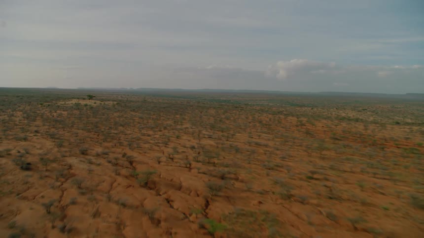 A dirt road is running through a dry desert plain under cloudy skies