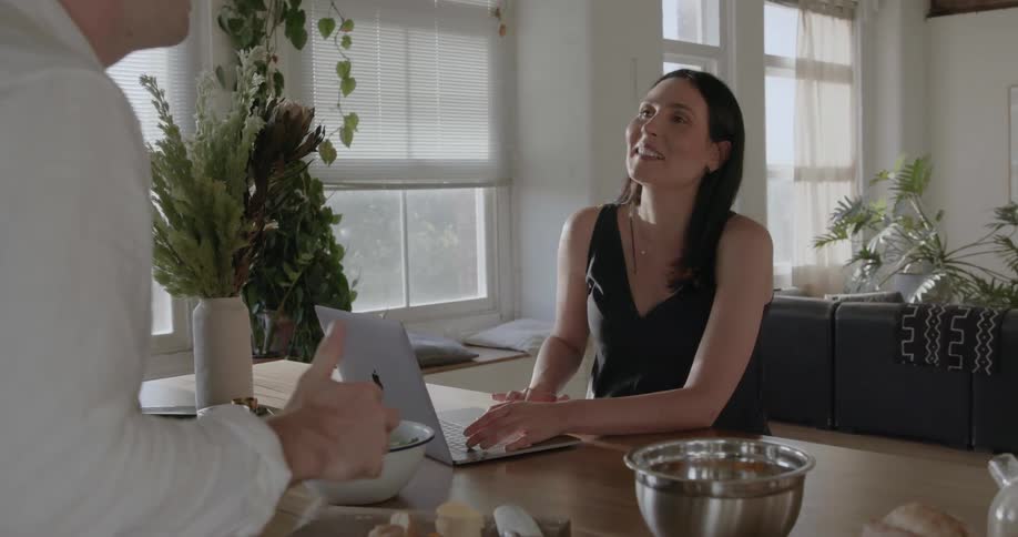 A woman looks up from the laptop talking to a man